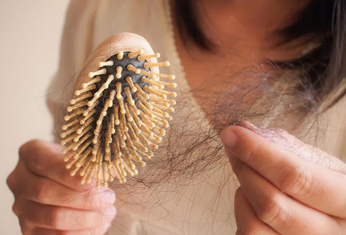 A woman holding a hair brush with hair strands.