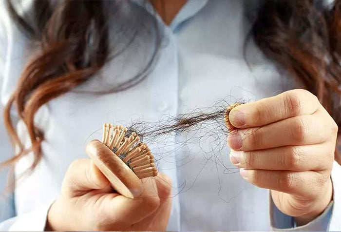 A woman pulling strands of hair from the hair brush