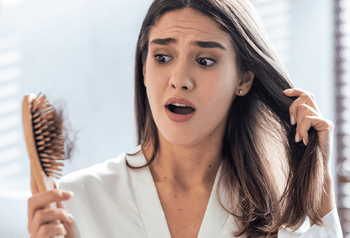 A distressed woman holding her hair and watching strands of hair on the hair brush