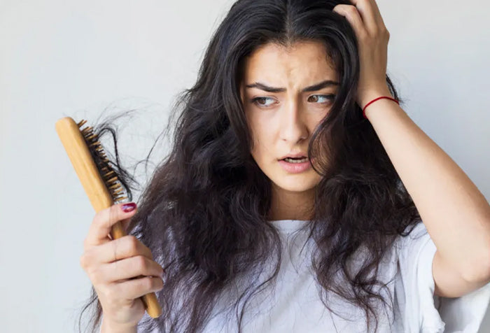 woman with a hair brush in her hand with strands of her hair, looking distressed